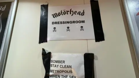 A sign saying 'Motorhead dressing room' with the setlist underneath