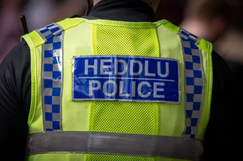 Getty Images A rear view of a male police officer on August 12, 2023 in Cardiff, Wales. he is wearing a luminous yellow vest with Heddlu written on the back in white on a blue background.