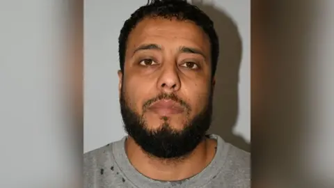 GMP A mugshot of Walid Saadaoui, who is wearing a grey t-shirt and has short dark hair and a dark beard. 