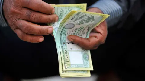 Getty Images Man counting Nepalese money.