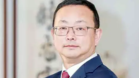 Yang Tengbo smiles at the camera, wearing glasses and a blue suit jacket.