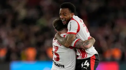 PA Media Two footballers players embrace as they celebrate winning a place in a play-off final