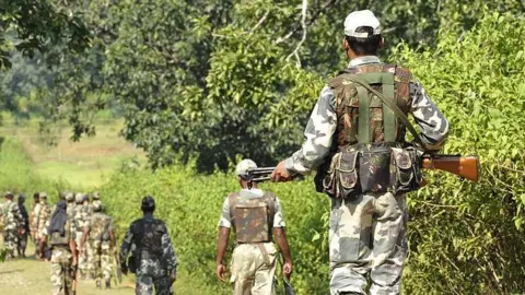 Armed security forces in khaki walk down a hill in a line