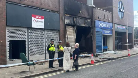 PA Media Two police officers stand outside the Citizens Advice officer. They are talking to two women stood on the other side of police tape. The office has been destroyed by the fire.