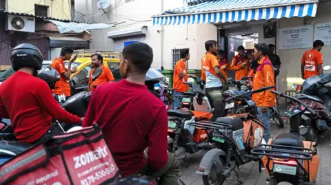 Bloomberg via Getty Images Swiggy and Zomato delivery workers in red and orange outside a dark store or warehouse in Mumbai, India. 