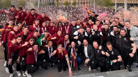 Bradford City players pose for a photo, with celebrating crowds behind them.