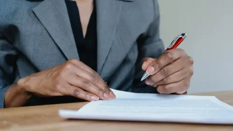 Getty Images a woman in business attire reviewing/signing documents at desk