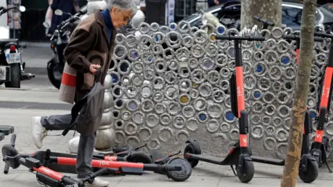 Getty Images A pedestrian steps over Voi's e-scooters in Paris