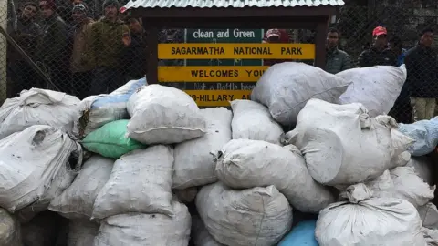 AFP Locals look at piles of rubbish bags lying against an airport fence next to a sign reading "clean and green: Sagarmatha National Park Welcomes You"