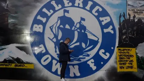 Jamie Niblock/BBC Jack stood in front of the Billericay Town mural, recording a piece for radio