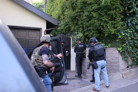 Los Angeles Police Department Four people from the LAPD Robbery Homicide Division wearing police vests and helmet approach the street entrance of a home belonging to singer David Antony Burke, who is known as D4vd.