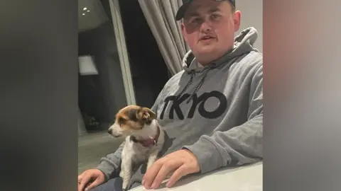 Bedfordshire Police Bobby Smith is wearing a grey hoody with a Jack Russell puppy sitting on his lap.