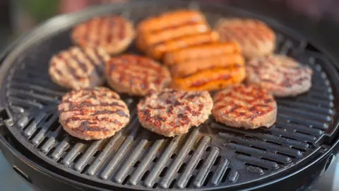 A metal grill with round burger meat patties being grilled on it.