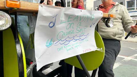 A hand drawn sign stuck to a beer bike saying "Leaving on a cruise ship - Don't know when we'll be back again"