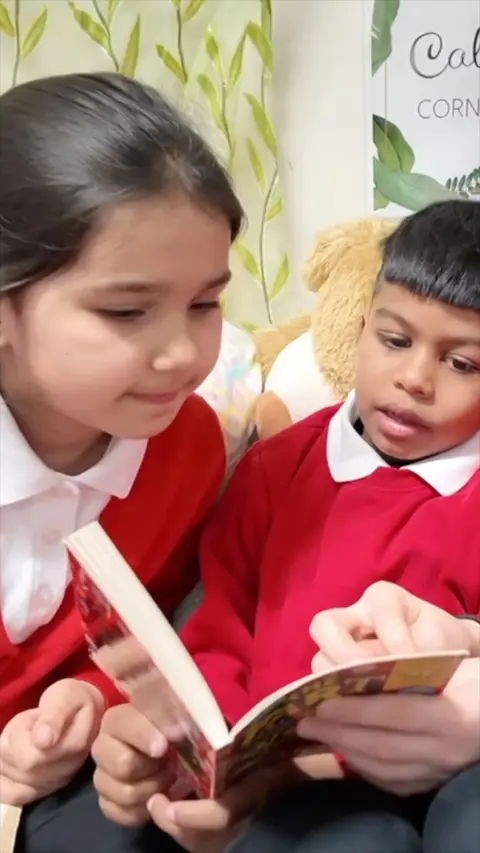 Two children in school uniform read a book.