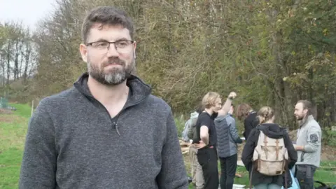 Picture of Dr Sandom standing in a meadow with students in the background.