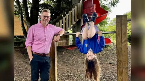 Blue Coat Primary School Headteacher Glyn Jones of Blue Coat Primary School wearing a pink shirt next to Flora, a year 5 student, in school uniform and upside down.