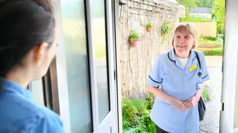 Dorothy House A Dorothy House Hospice Care staff member on the doorstep speaking to a woman at her home.