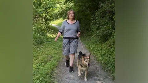 Sarah Robinson walking her dog Dylan in the Ironbridge Gorge, along a path flanked by trees