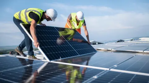 Two men in hard hats and high vis installing a solar panel 