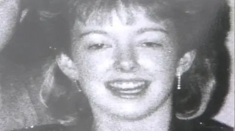 A black-and-white photograph of Diane Sindall, who has her hair cut into a fringe. She is smiling at the camera.