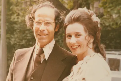Eva and Herbert King Herbert and Eva standing next to each other. Herbert is wearing a brown suit and tie and Eva is wearing a white top