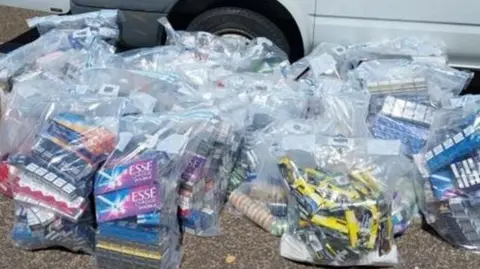 Kent Police Multiple bags of illegal vapes and cigarettes lie on the ground