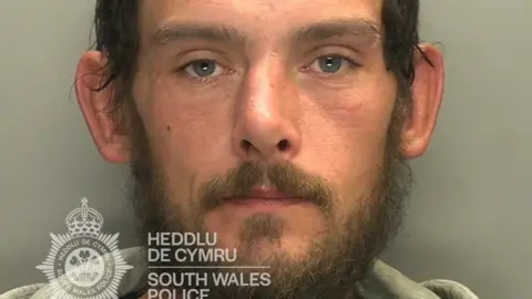 Mugshot image of 33-year-old Lee Jakes, sentenced to 16 months in prison for arson at Cardiff Crown Court on 23 June. He has a brown beard and blue eyes and wears a grey hoodie.