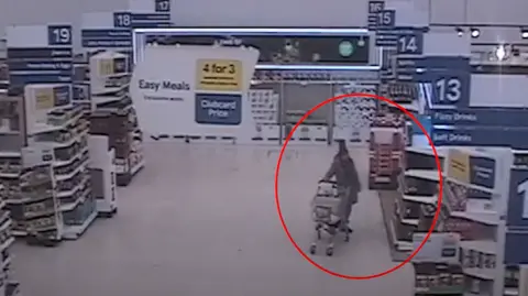 CTV image of a woman standing next to a shopping trolley in a supermarket aisle 