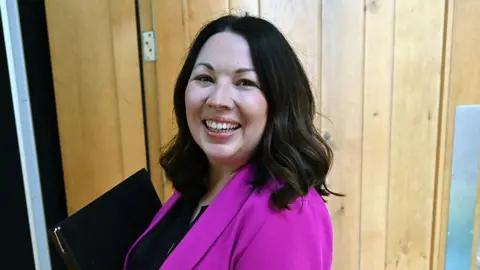 Getty Images a smiling woman with shoulder-length black hair is wearing a pink jacket