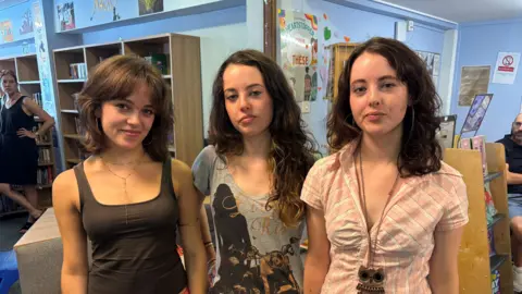 Emily Holt/BBC Three people stand side by side inside a classroom.