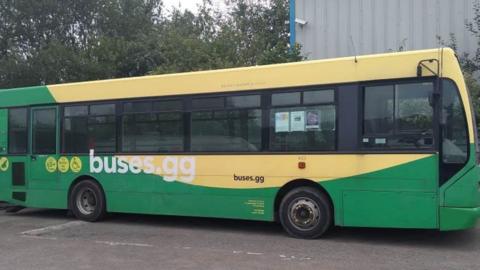 A green and yellow bus with the web address buses.gg on the side. 