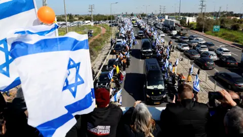 Reuters Israelis have been depicted holding Israeli flags and orange balloons, a convoy in the form of a convoy that takes the coffins of hostage Shiri, Ariel and Kefir Bibas, makes its way from Central Israel to South Israel (26 February 2025)