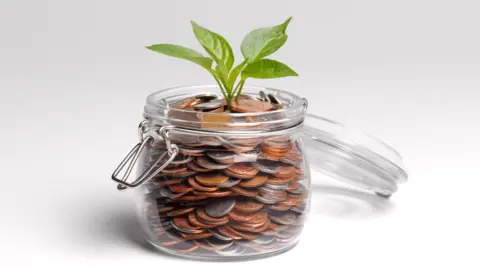 A stock image of a glass mason jar filled with 1ps and 5ps and a small plant coming out of the top.