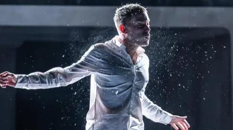 Marc Brenner Scene from Punch showing a man shaking water droplets off his body, clad in a white shirt.