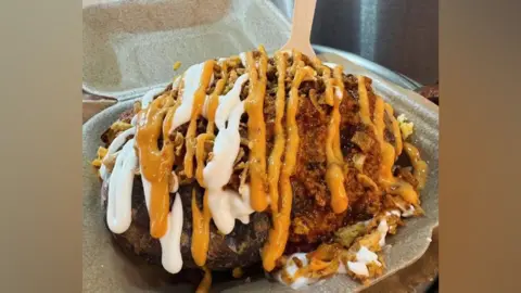 Spud Bros A loaded jacket potato doused in white and yellow sauce on a grey tray