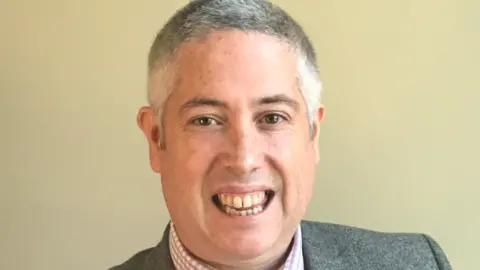 A head-and shoulders image of a man with grey hair