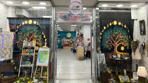 Alice Cullinane/BBC The outside of Shop in the Square with fairy lights in the shop window and curtains with tree patterns. 