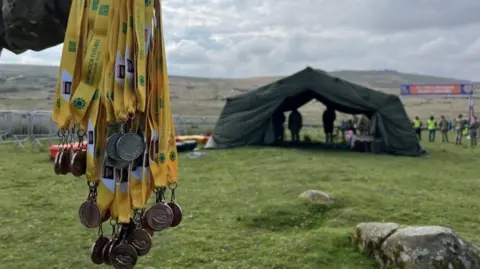 The Ten Tors medals being held in front of the finish line.