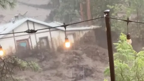A house is swept along a brown river of raging flood water.