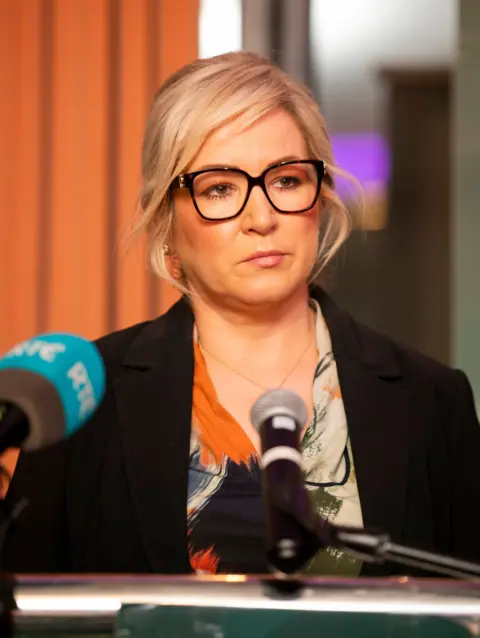 Michelle O'Neill, a blonde woman in black glasses, at a press conference