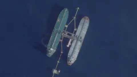 An overhead view of two oil tankers at sea, docked next to a pipe