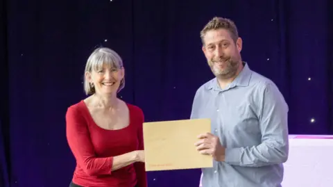 Rogan Productions Tina on the left collects her BSL level 1 certificate from a man wearing a blue shirt