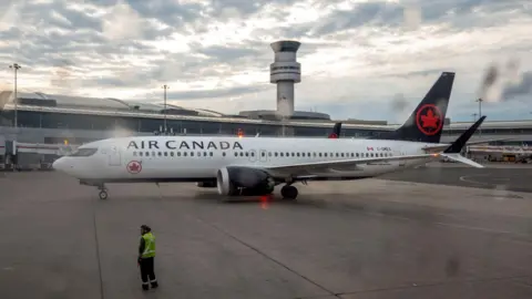 Reuters Air Canada plane sits on a runway with an air traffic control tower in the background.