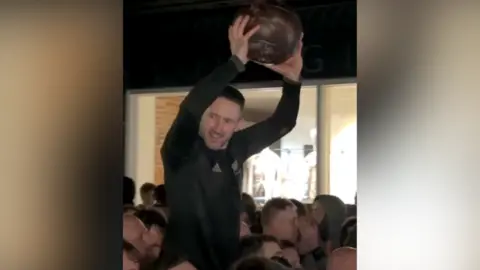 Craig Brown holding the Royal Shrovetide Football in the air whilst being carried to the Greenman pub in Ashbourne