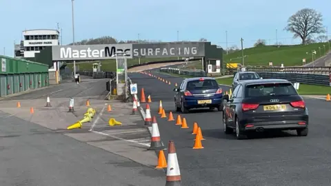 Two cars driving past some cones on a racing circuit