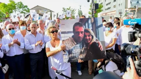 AFP Wife of bus driver Philippe Monguillot, Veronique Monguillot (centre) holds a portrait of her husband during a march in Bayonne, France. Photo: 8 July 2020