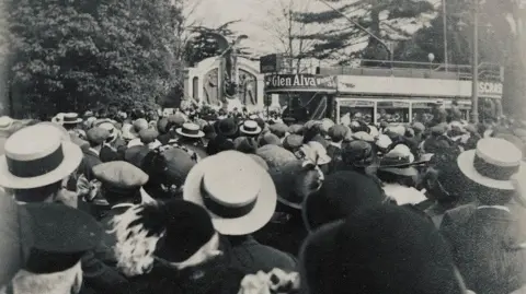 Mike Thomas A black and white image of a large crowd gathered in front of the new Titanic Engineers' Memorial in 1914. Next to the memorial is a large double-decker bus.