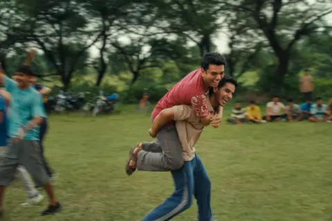 Dharma Productions A still from the film Homebound which shows a man carrying another man on his shoulders on an open field