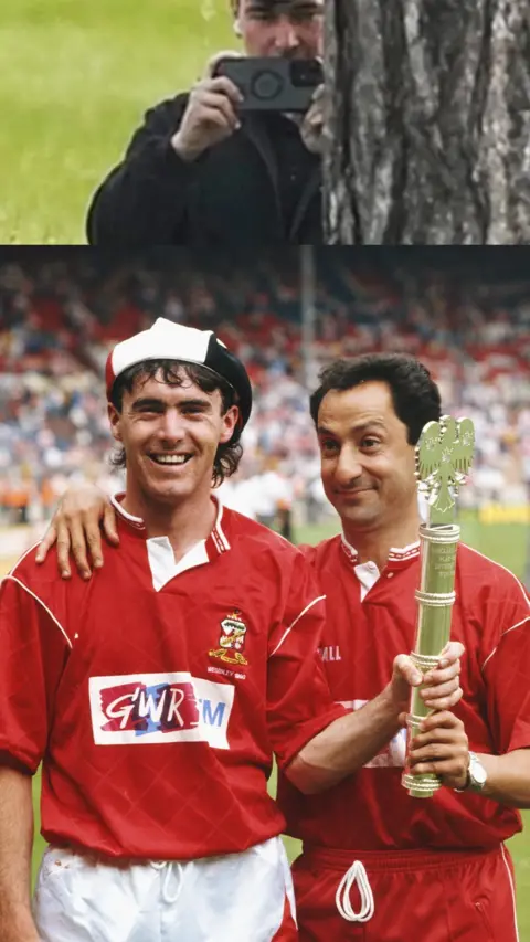Two Swindon Town FC players stood in red T-shirts and holding cup